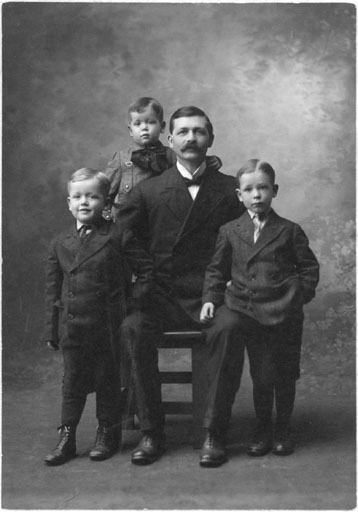 Photograph from about 1907 of Archibald Ralph Collins seated with his three sons around him.  James Cummins Collins is standing on the right, Sterrett Cummins Collins is standing on the left, and John Oliver Collins is standing behind.
